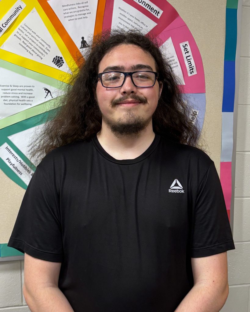 Person in glasses smiling in front of a rainbow colored wheel.