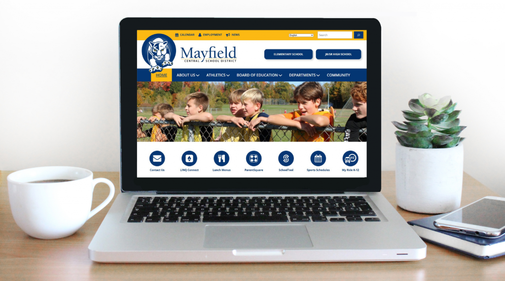 desk with cup of coffee, plant, phone and laptop with Mayfield website displayed