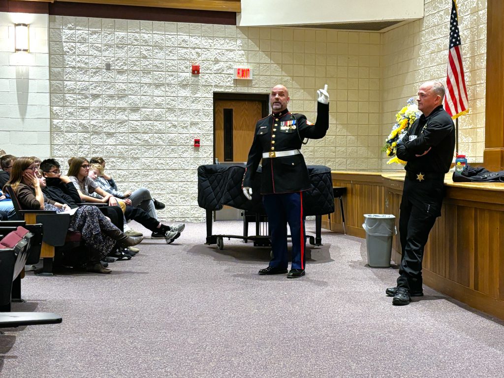 Man in military uniform speaks to students as another officer looks on.