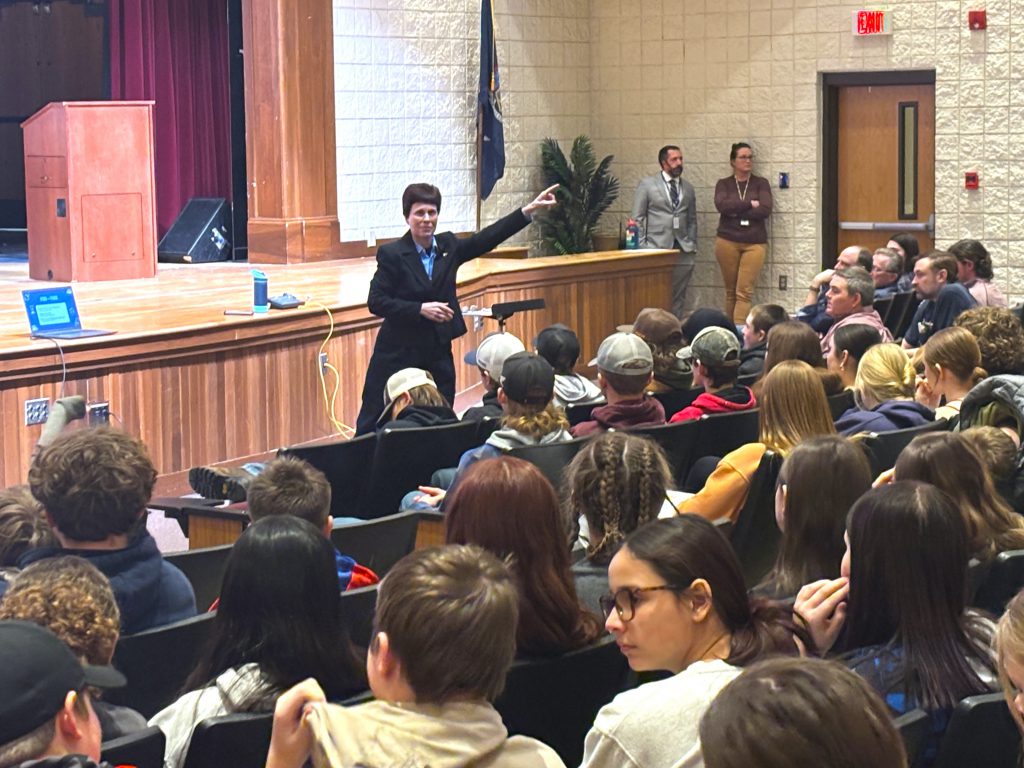 a woman points as she stands in front of an auditorium of students