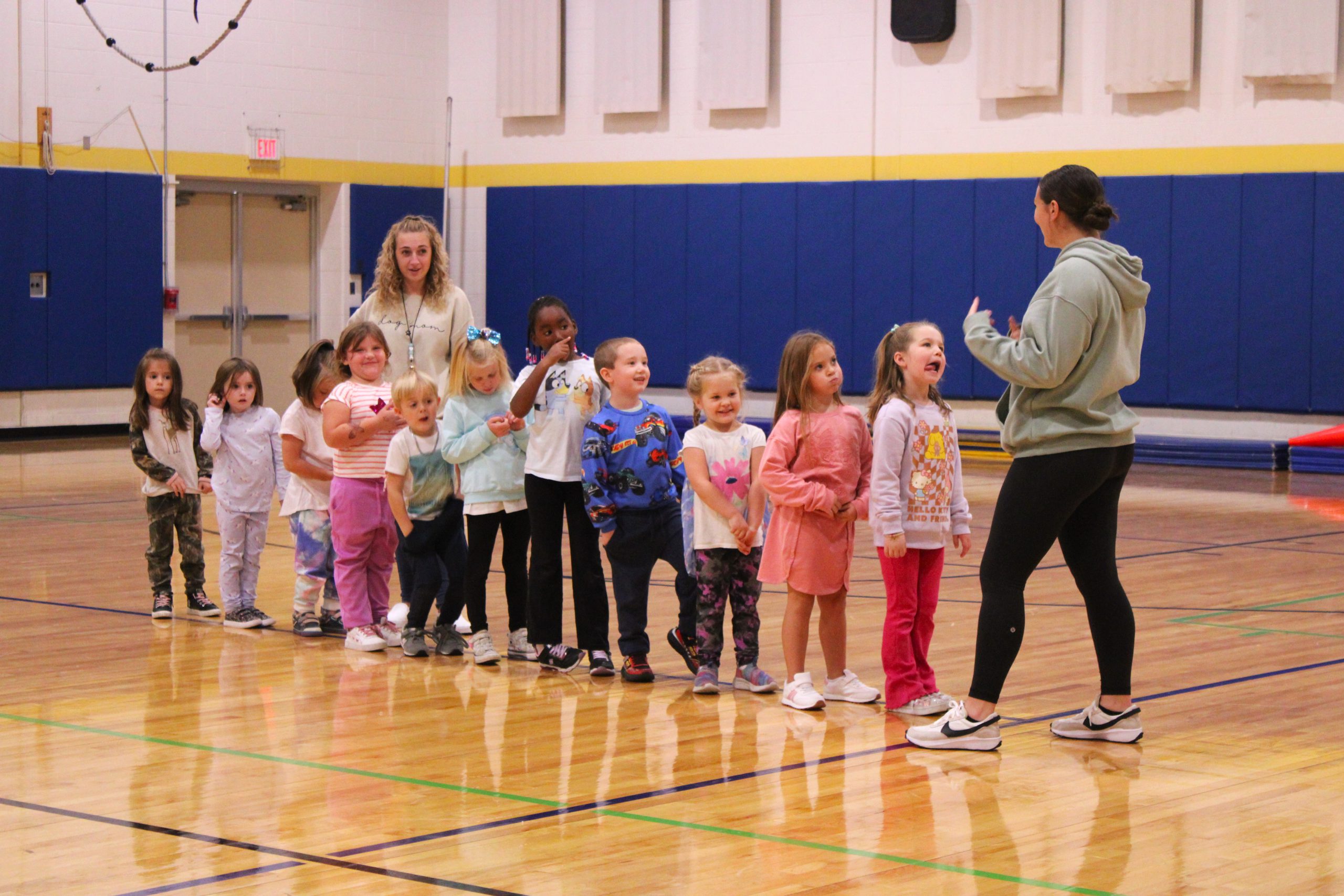 students stand in line in gymnasium with a teacher at the front