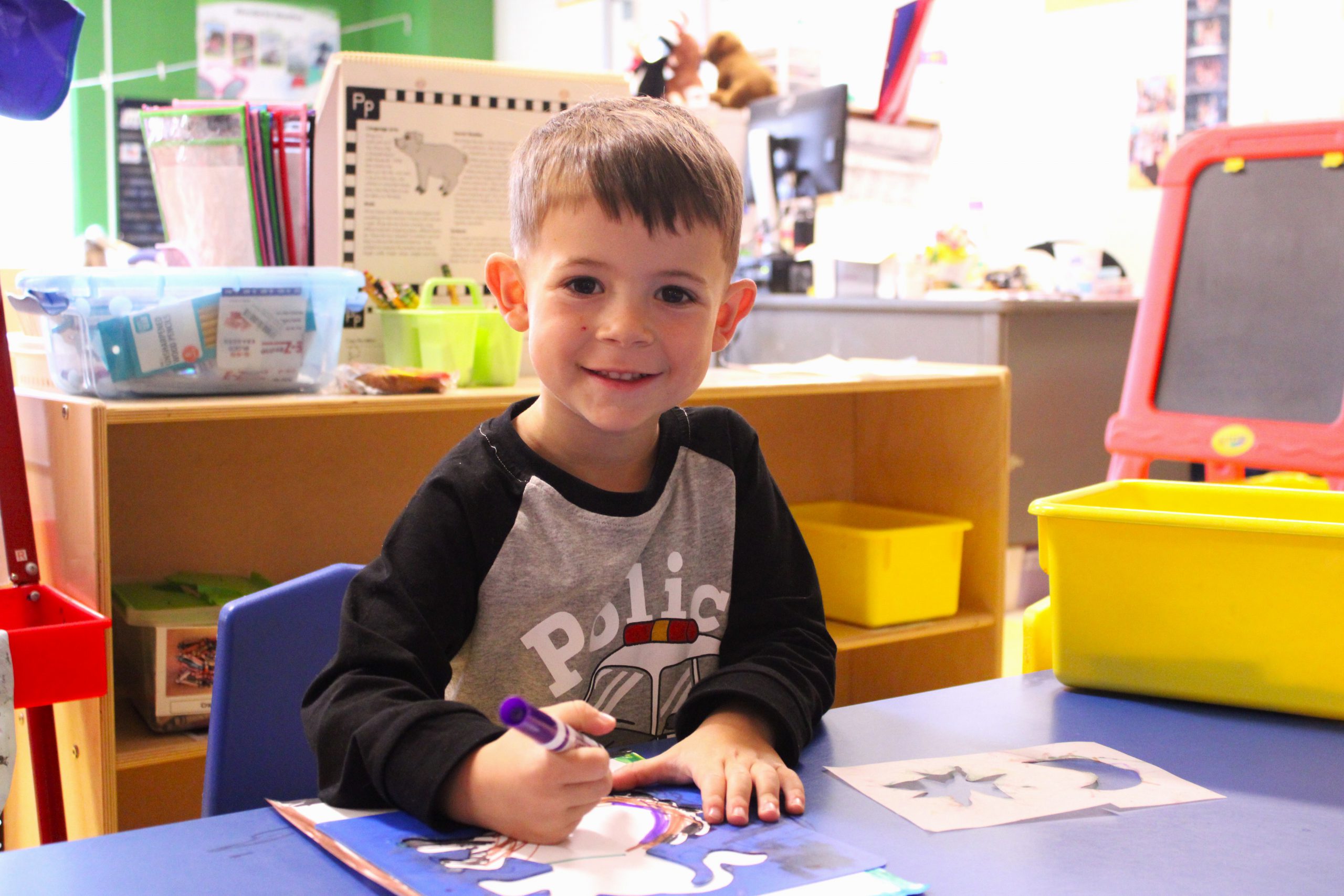 little boy colors and smiles at the camera