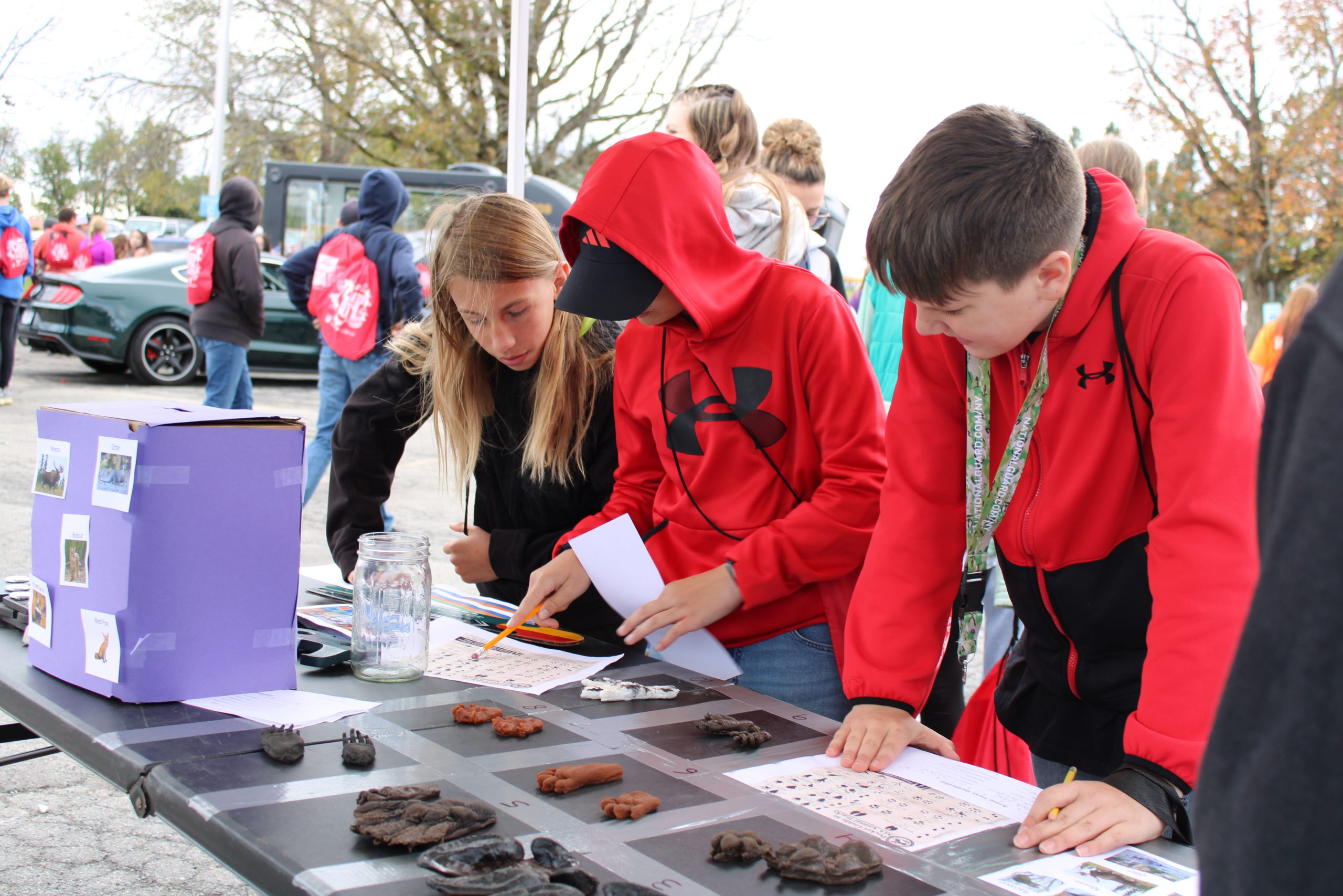 three students lean over table and identify objects