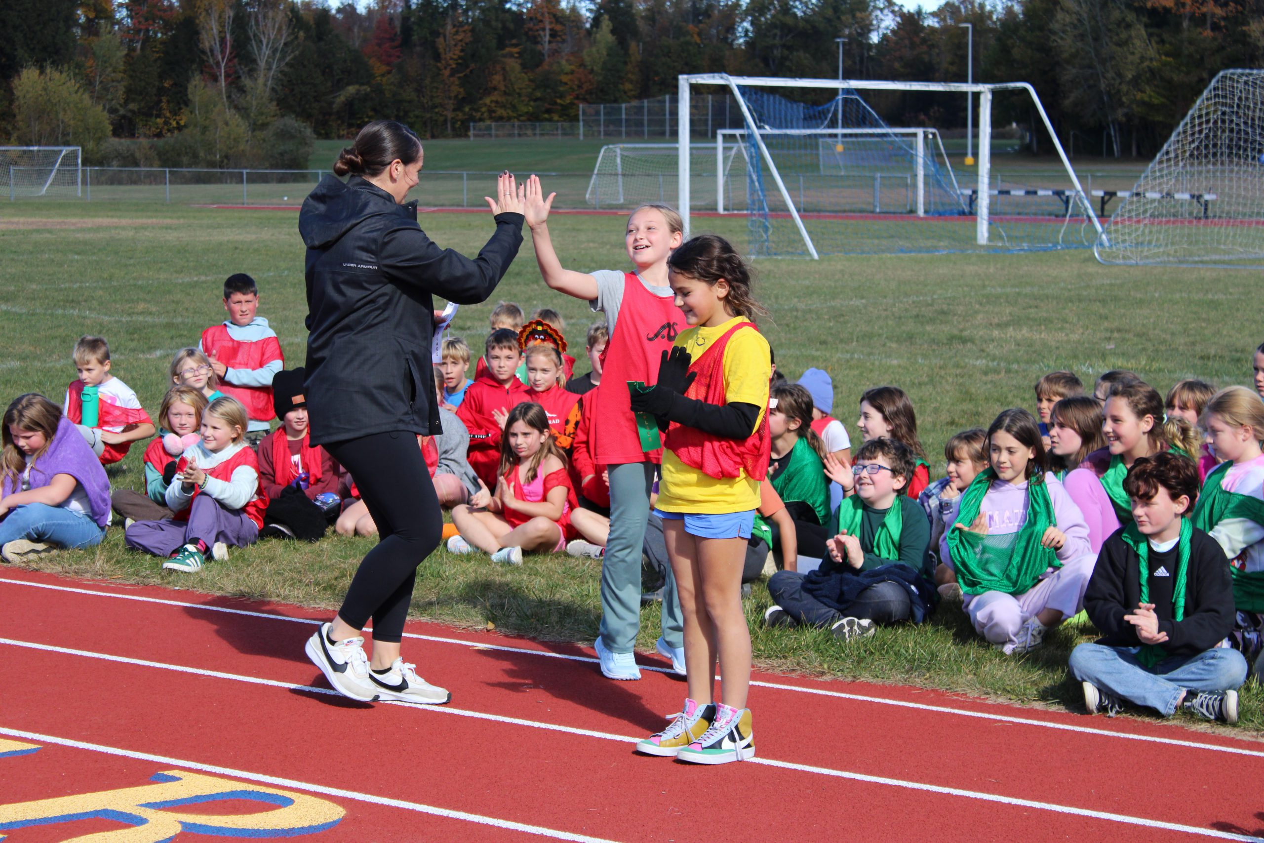 gym teacher high fives girl in red uniform while other classmates looks on