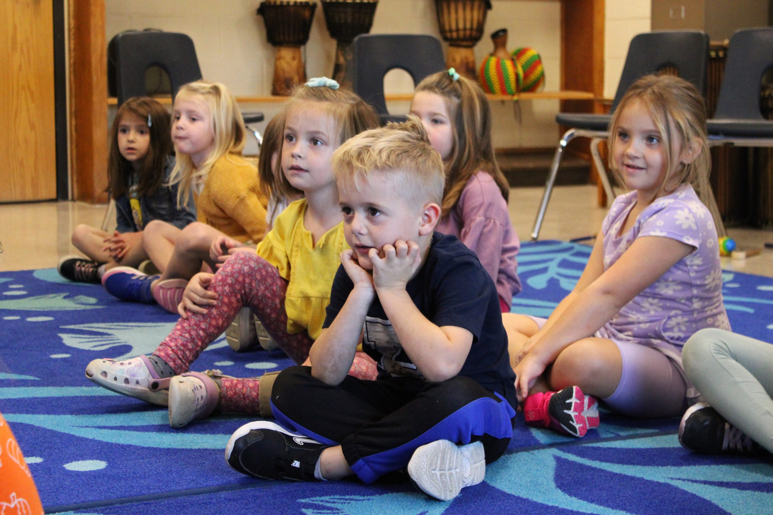 small children sit on a rug and listen to the teacher