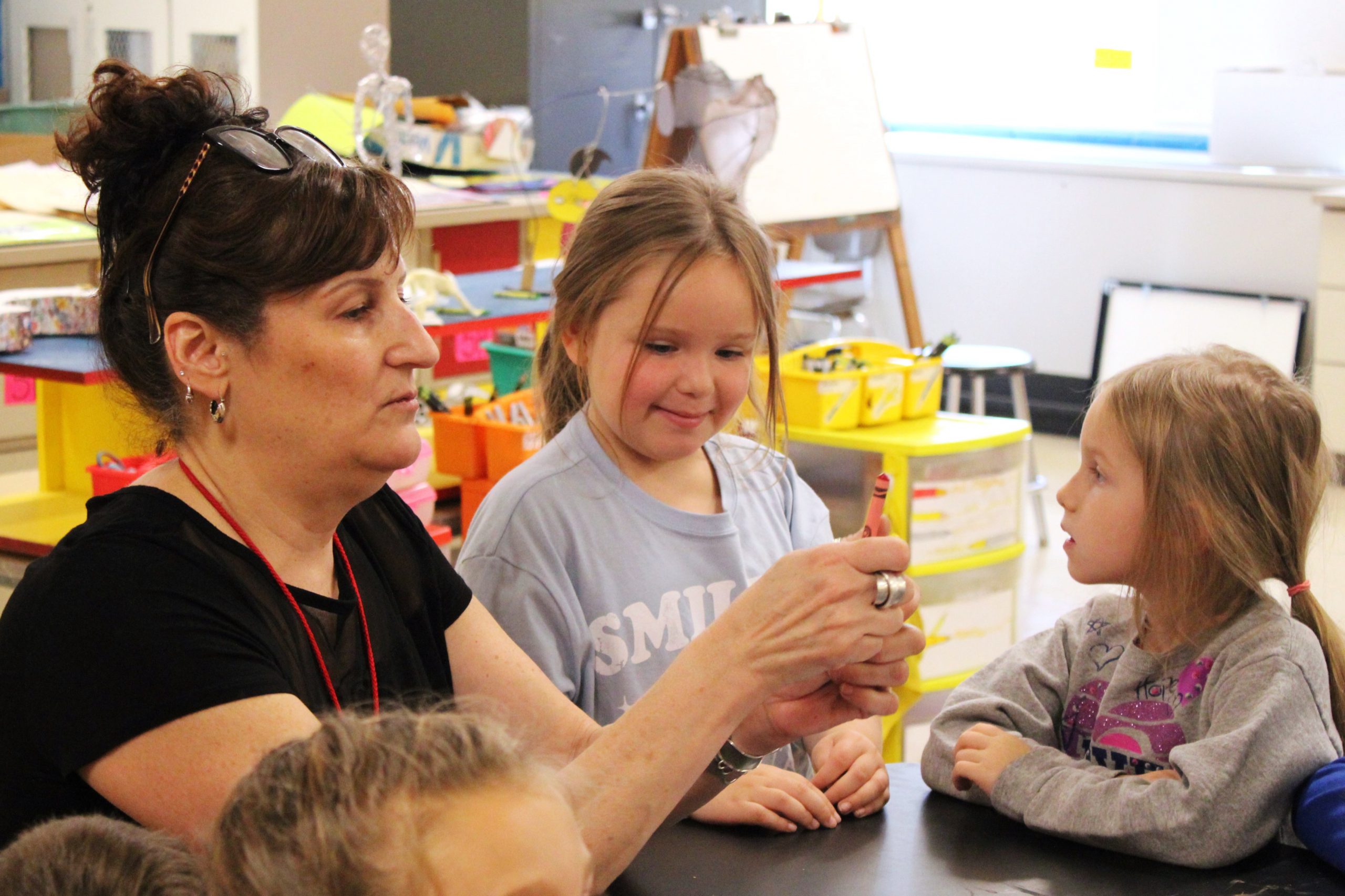 art teacher shows different crayon colors while students look on