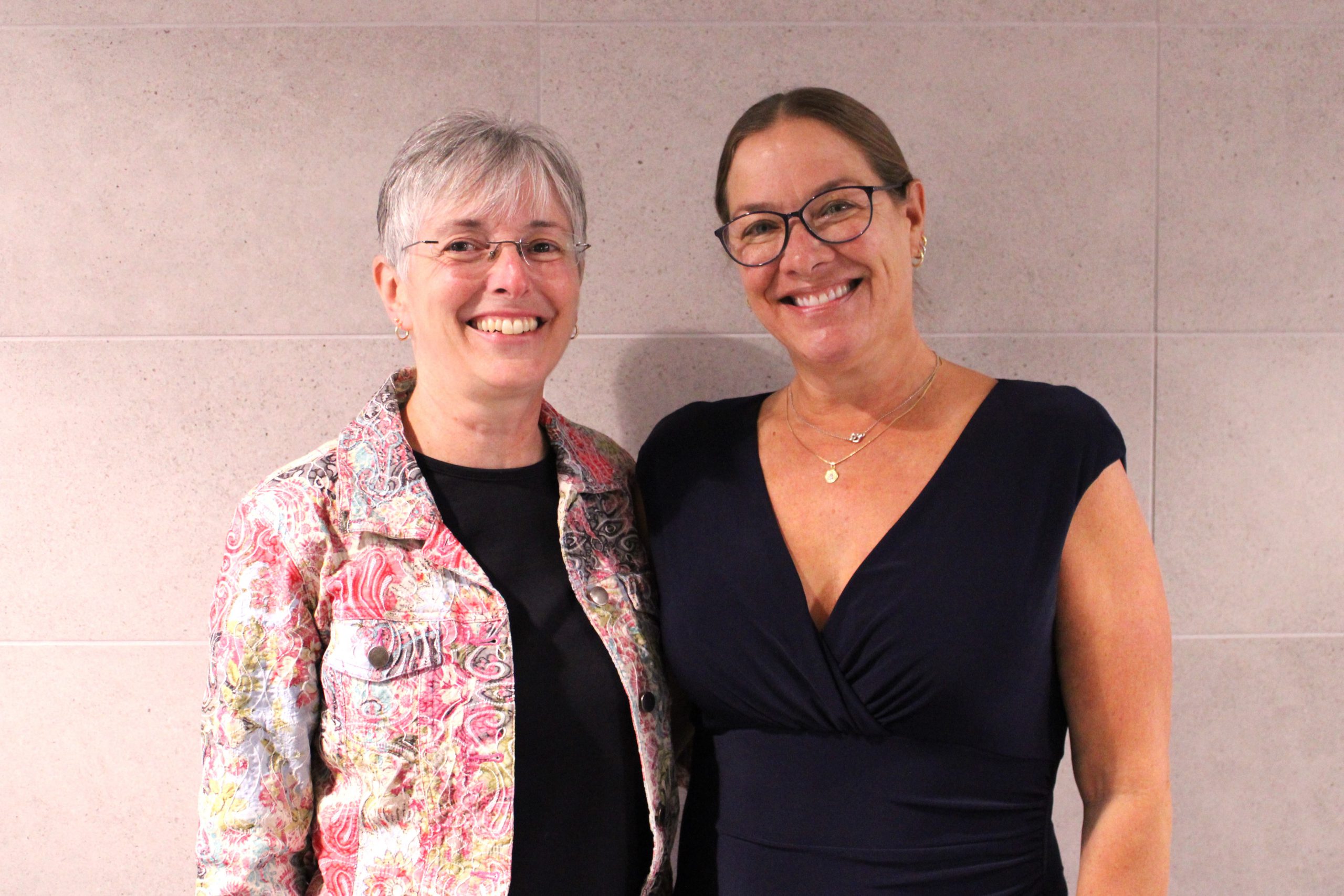 Two women stand together and smile.