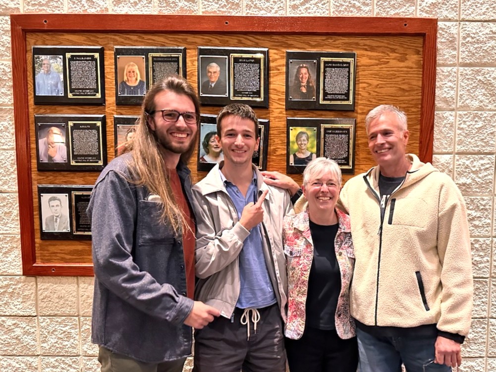 Four people stand together in front of a wall of plaques.