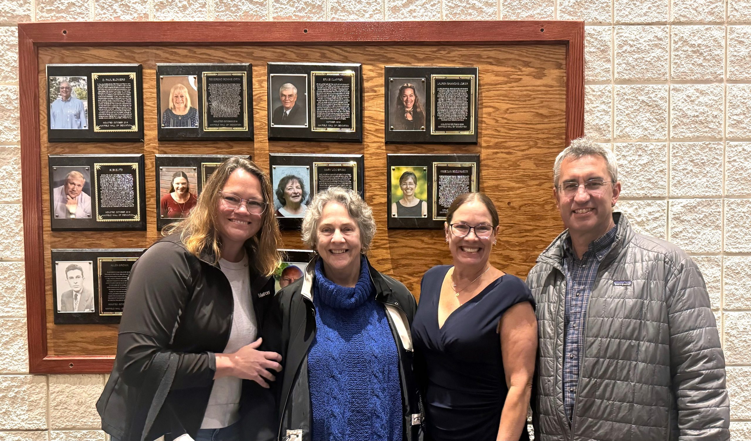 Four people stand in front of a wall of plaques